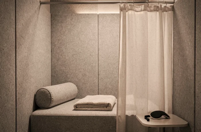 Espace micro-sieste dans une salle de pause avec banquette rembourrée, rideau occultant et coussin de repos