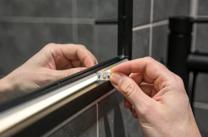 Gros plan de mains collant une nouvelle bandelette LED sur le cadre arrière d'un miroir de salle de bain